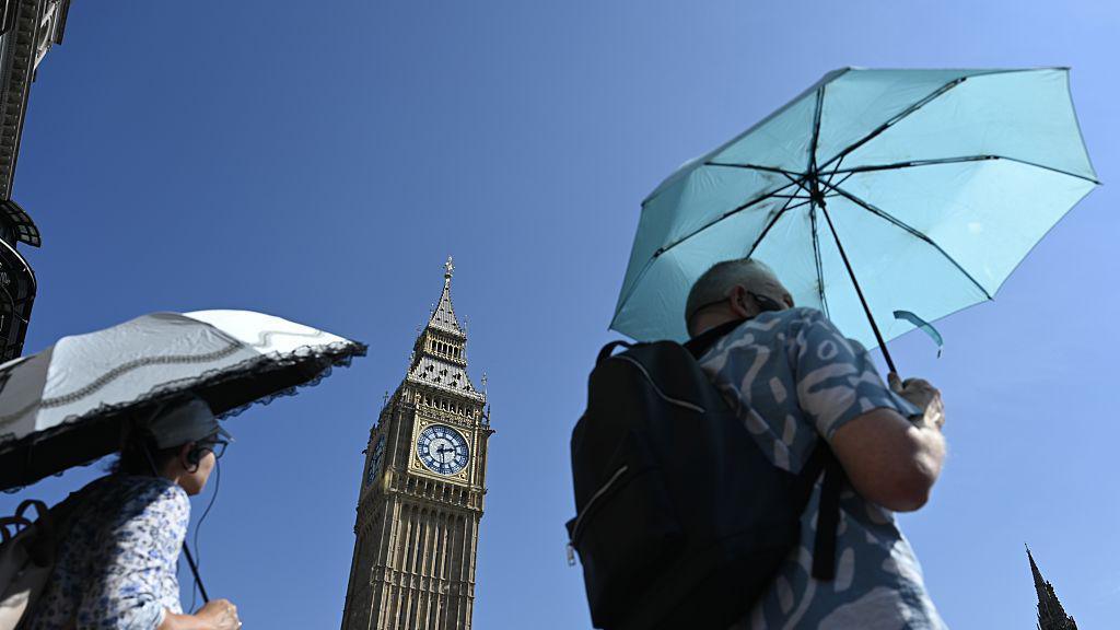 A man using an umbrella to shield himself from the sun near Big Ben.