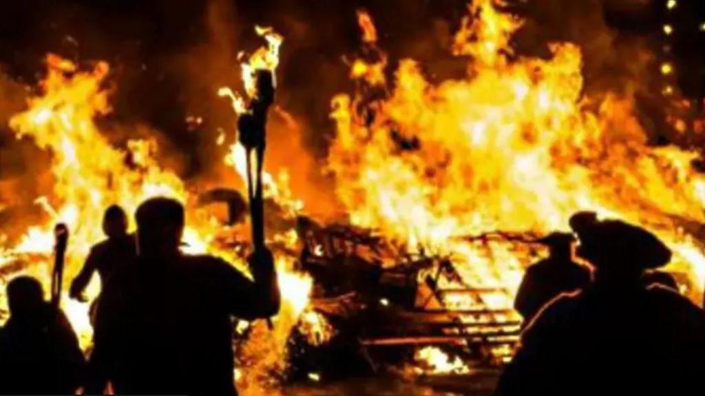 People in shadow carrying torches in front of a large bonfire with huge flames in Littlehampton