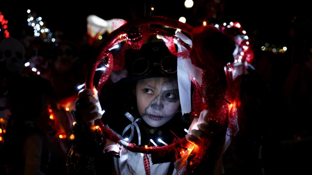 A child with face paint is holding a red circle with lights 