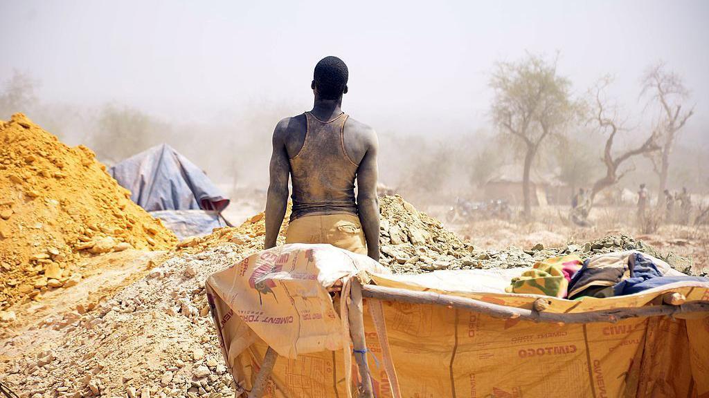 A man stands with his back to the camera, looking at a clandestine gold mine in Burkina Faso