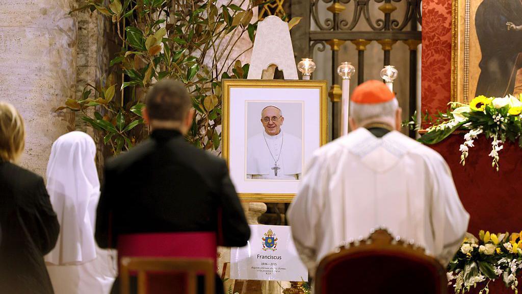 Mourners stand in front of a framed photo of Pope Francis outside St Mary Major basilica in Vatican City.