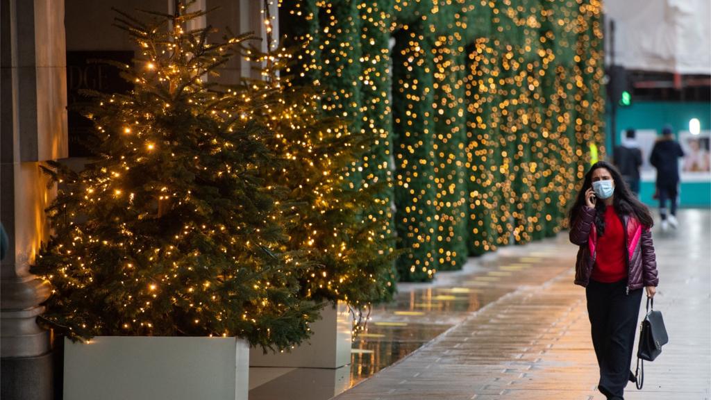 People walk past Christmas lights outside a closed shop on Oxford Street, London. Prime Minister Boris Johnson cancelled Christmas for almost 18 million people across London and eastern and south-east England following warnings from scientists of the rapid spread of the new variant of coronavirus.