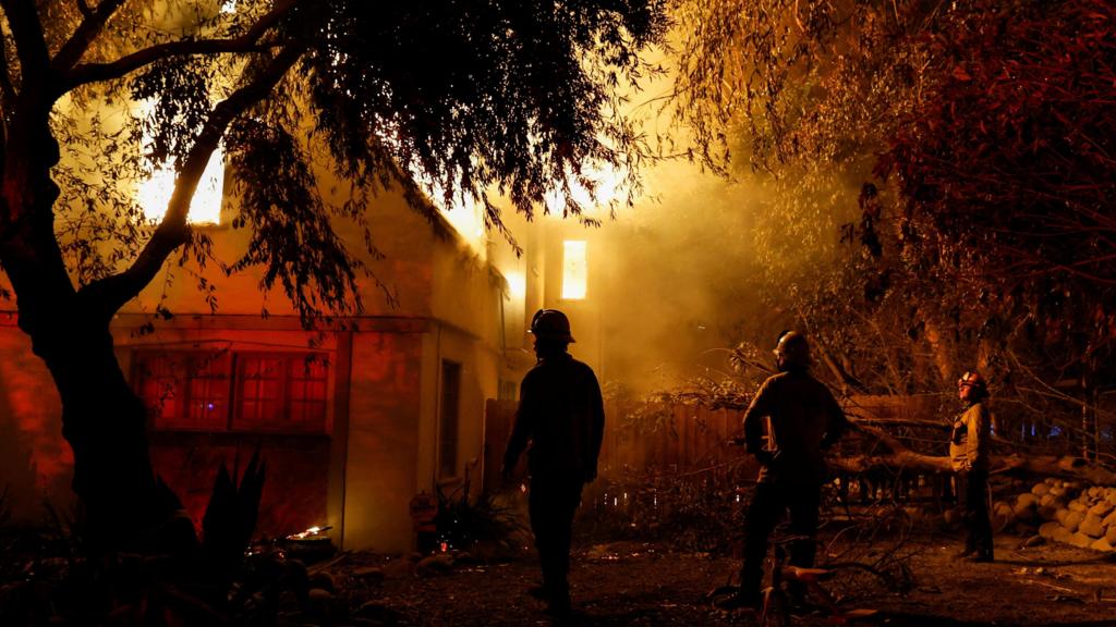 Firefighters lit up by a blaze in a house inspect the damage