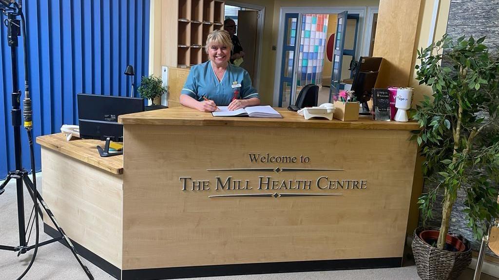 Maria swears and nurses outfit and stands behind a fake GP desk on the set of Doctors. 