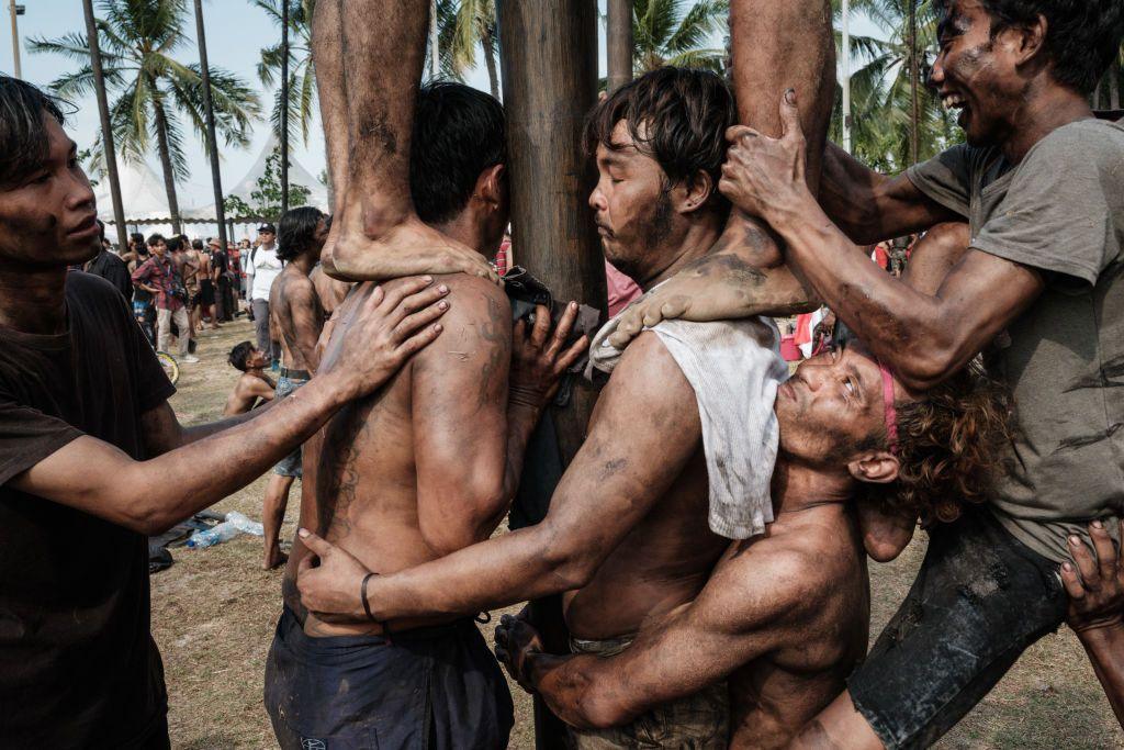 People covered in grease attempt to climb a greasy pole