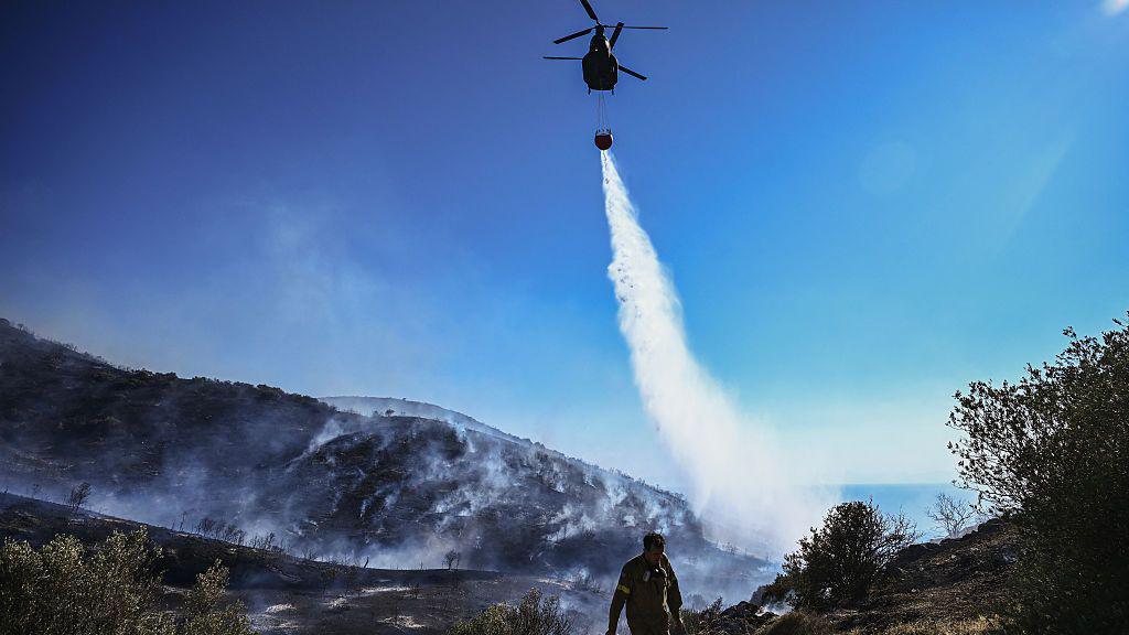 A firefighting helicoter Sikorsky S-64 Skycrane drops water on a forest fire, near Thymari, southeast of Athens, on June 26, 2025