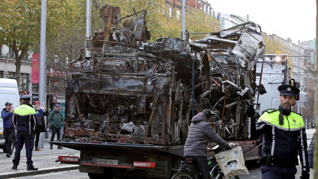 The shell of a burnt out bus is pictured on a truck as it is removed O'Connell Street in Dublin on November 24, 2023, following a night of protests.