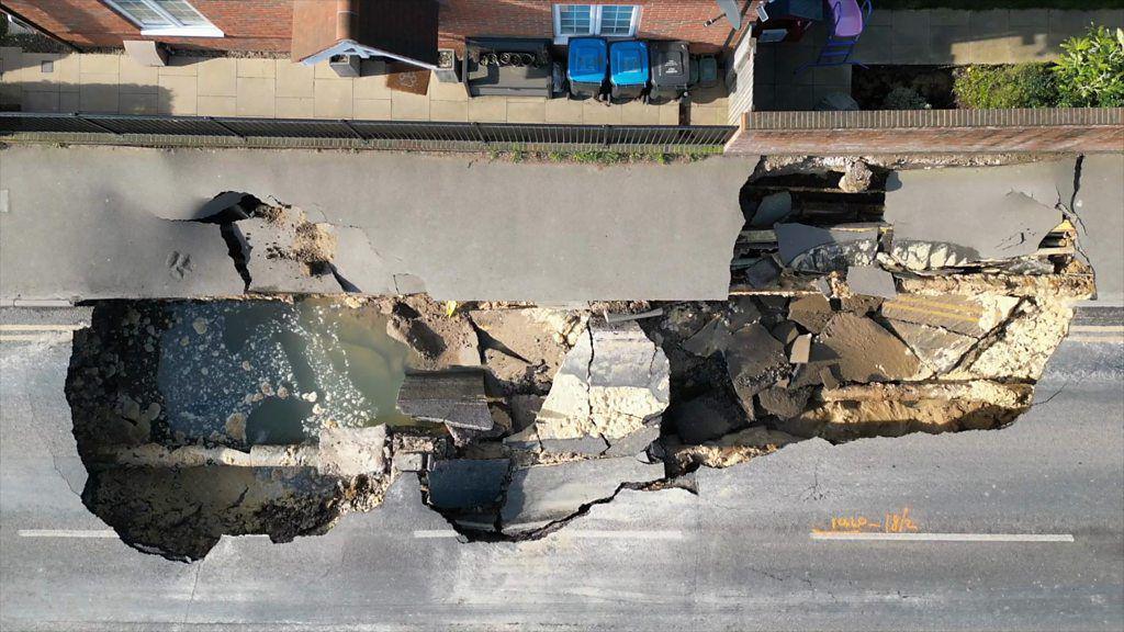 An aerial view of a 60ft sinkhole in a stretch of road with water in the bottom