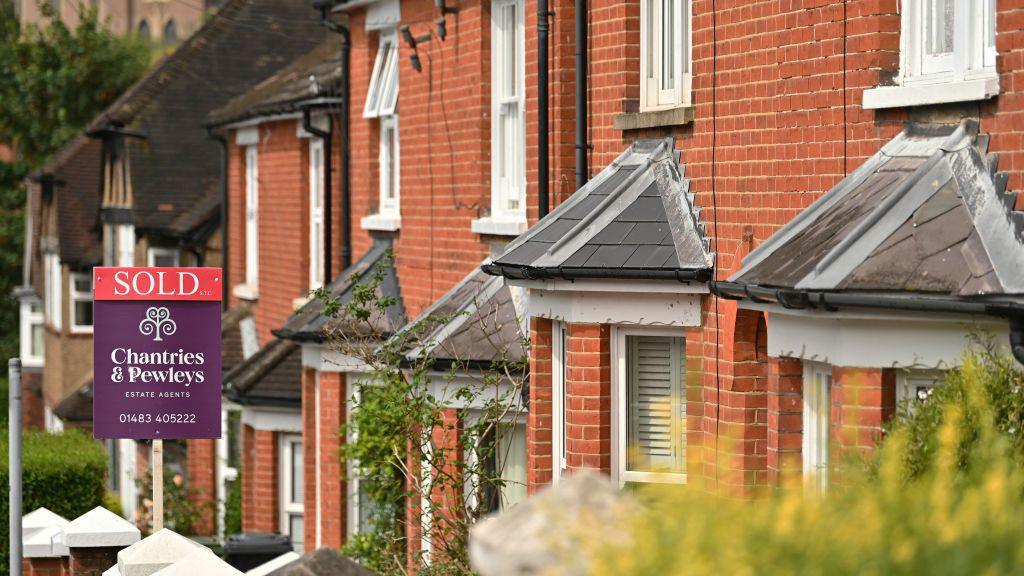 A street of Victorian red-brick houses in Guildford, one with a "Sold" sign outside.