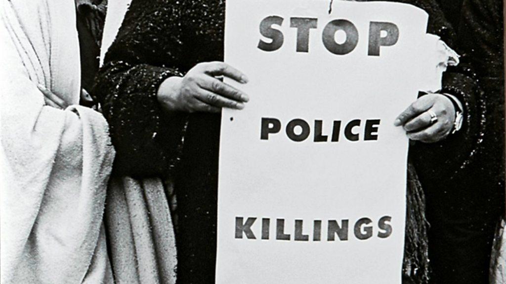 A woman holding a sign 'Police Stop Killing' taken from the book 'The Fire Next Time' by James Baldwin