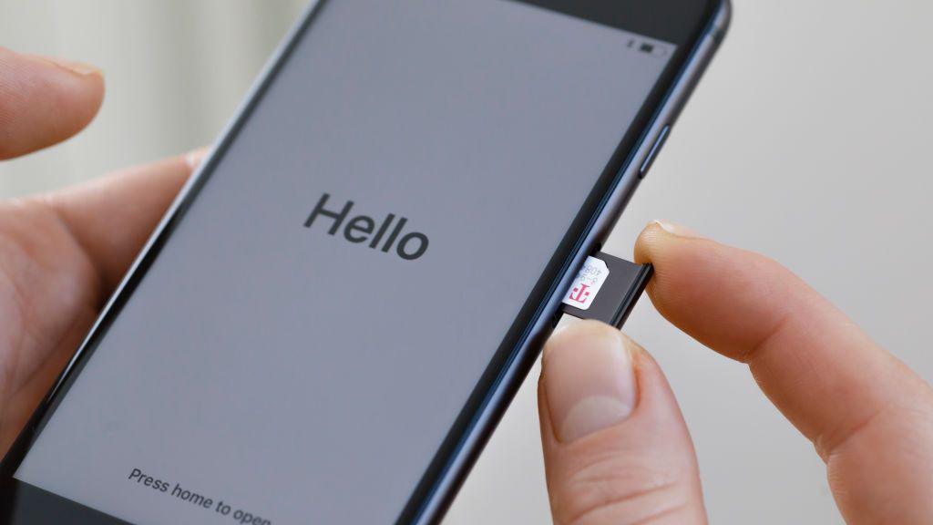 A person pushing a sim card into a mobile phone. On the mobile screen, it says 'Hello'