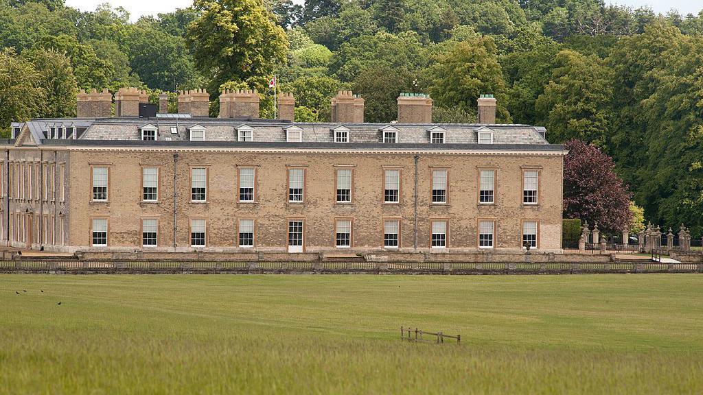 A large stately home with a field in front of it and trees behind it.