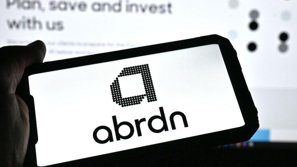 Person holding a phone with the Abrdn logo on it