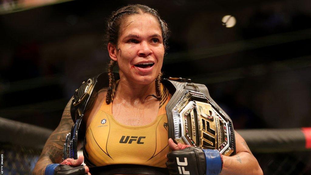 Amanda Nunes holds her bantamweight and featherweight title belts