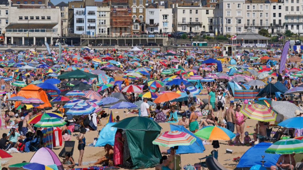 Busy beach with people laying on the san sunbathing under their colourful sun umbrellas