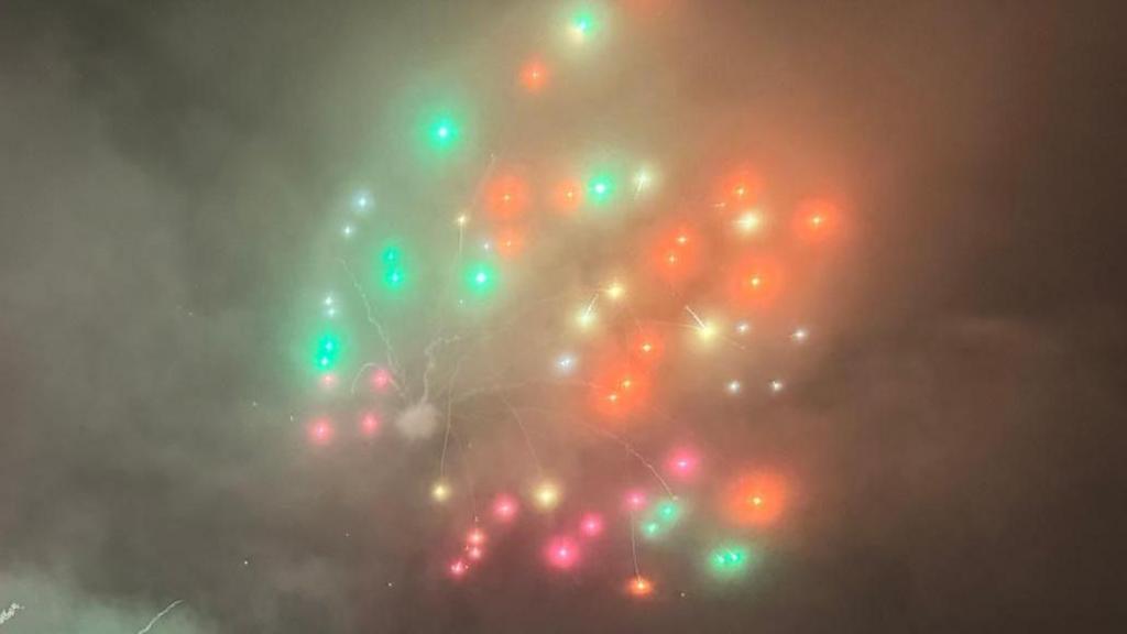 A firework emitting colour of green, white, yellow and orange sparkles after exploding in the night sky.