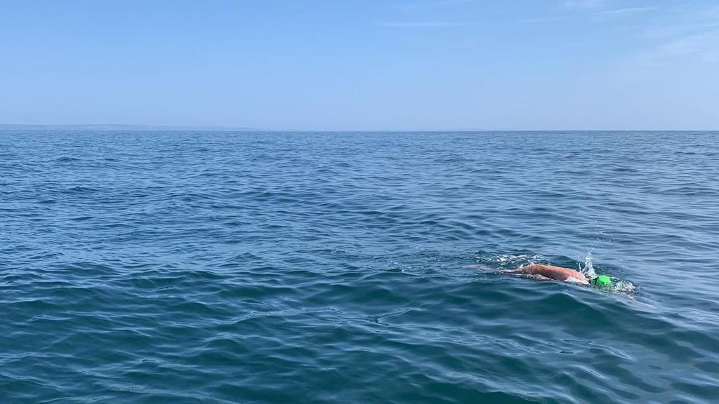 A man in a green swimming cap swimming in the sea.