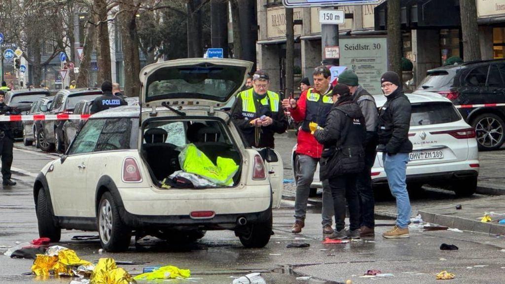 Officers inspect the car - a cream mini cooper with its boot open - with debris strewn across the road underfoot.