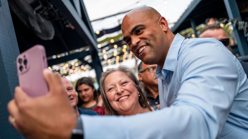 Colin Allred, wearing a blue button-up shirt, takes a selfie with a supporter in Texas