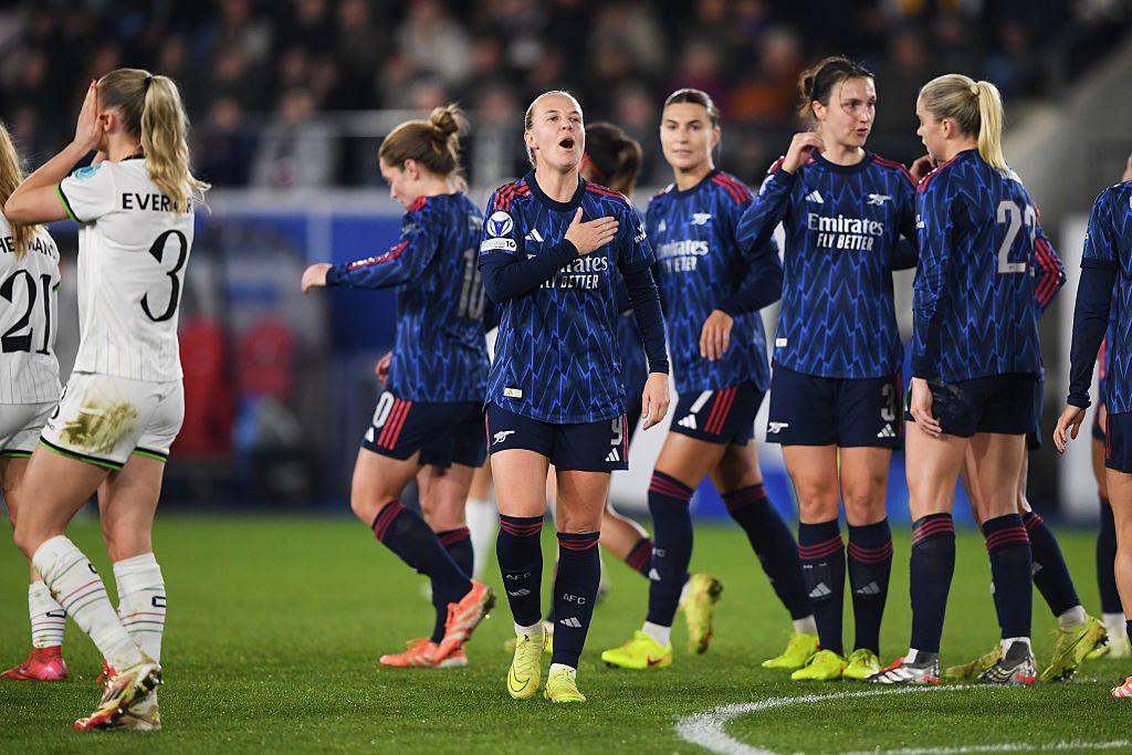 Beth Mead, in Arsenal's blue and black away kit, celebrates with a hand over her heart while other Arsenal players stand around her