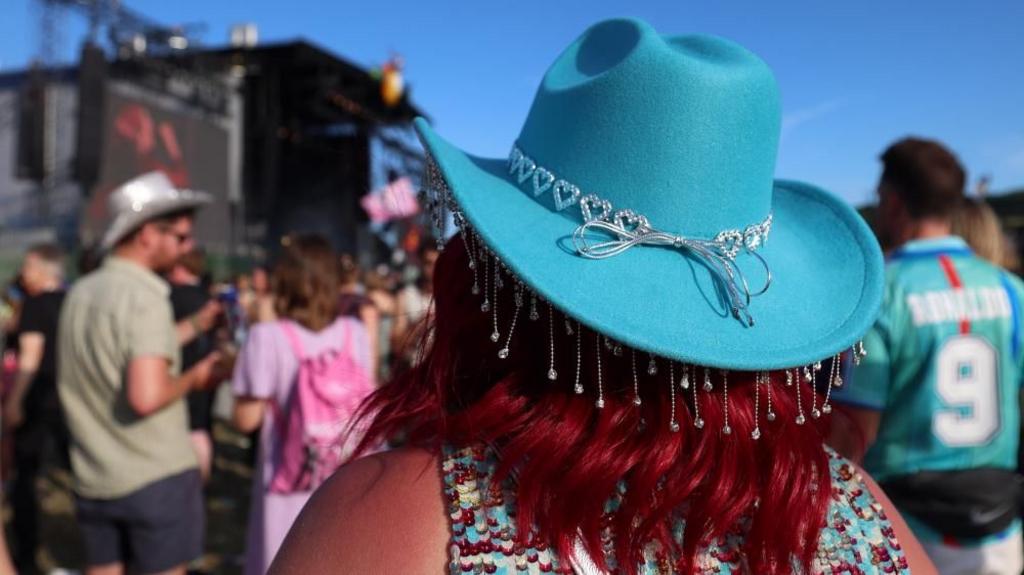 The back of a woman's head at Glastonbury - she wears a bright blue cowboy hat decorated with a string of diamonte hearts
