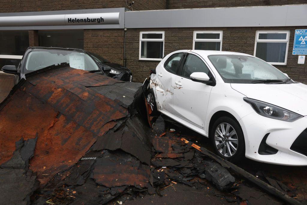 Debris that looks like it has been blown from a roof strewn on top of a black car. A white car sitting next to it has also been damaged