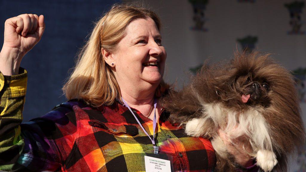 woman holding up hairy dog with sticking out tongue