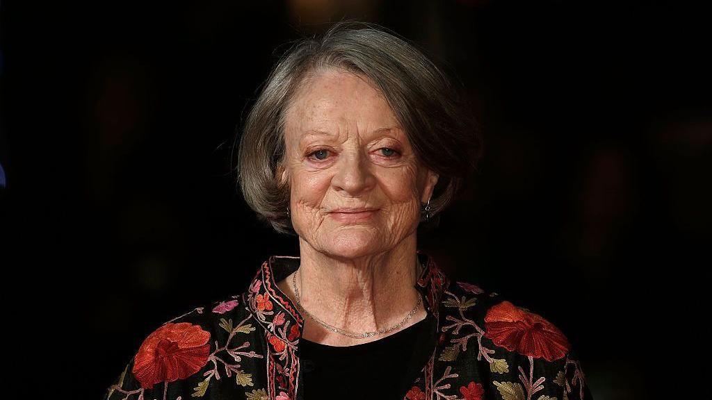 Dame Maggie Smith smiles against a black backdrop