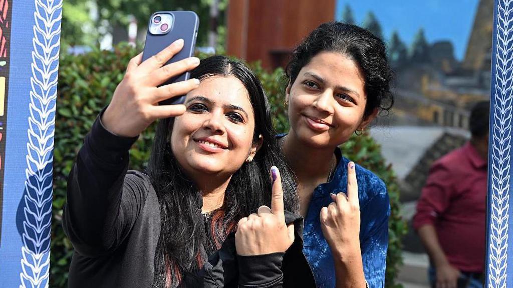 Two women click a selfie outside a polling booth in Bihar's capital Patna with inks on their fingers that show they have cast their votes.