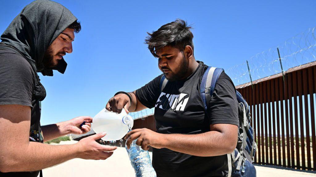 Migrants from India share water in the intense heat after walking into the US from Mexico at Jacumba Hot Springs, California, on June 5, 2024. 