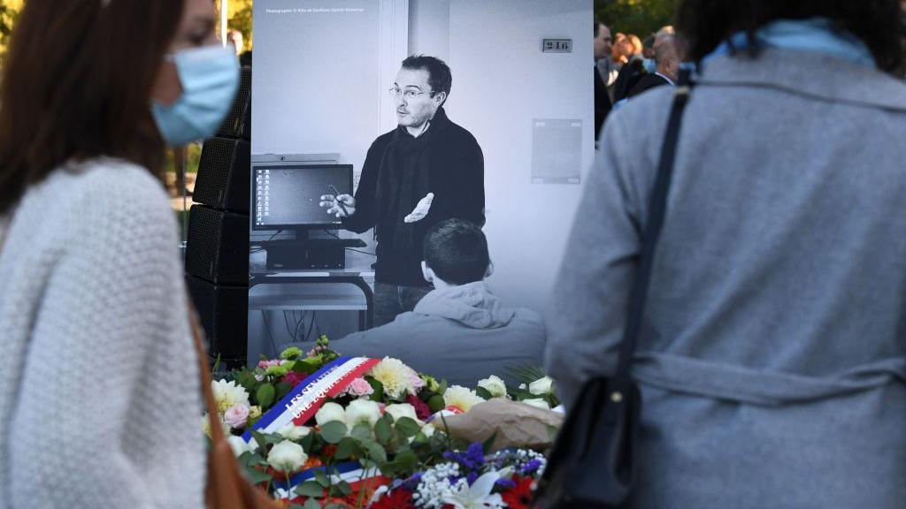 Mourners pause outside a tibute showing a grey-and-white photo of French high-school teacher Samuel Paty 