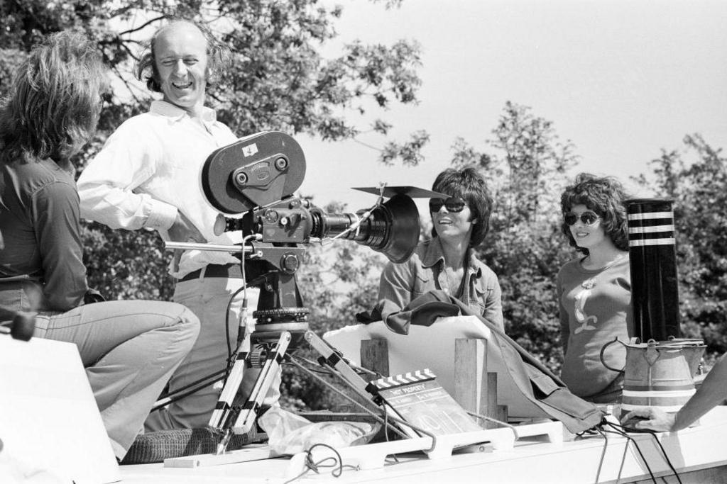 Sir Cliff Richard and an unnamed actress are being filmed by a production crew on a narrow boat. The actors are both wearing dark glasses and looking towards the film camera
