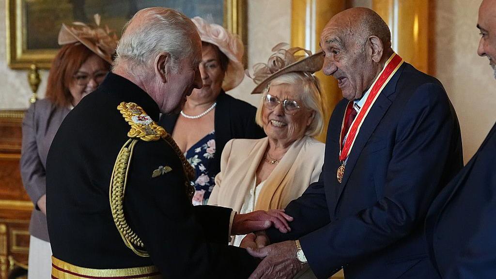 Sir Billy Boston shakes the hand of King Charles III before being knighted