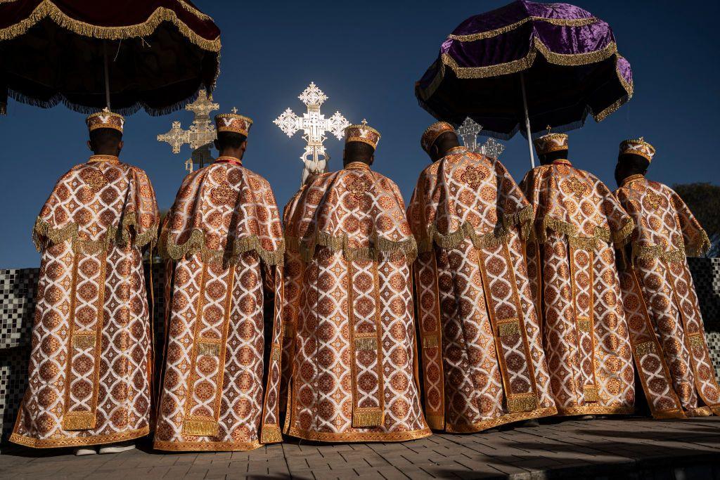 Clergy wear embroidered robes and carry large, ornate crucifixes.