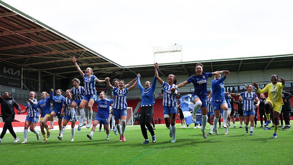 Brighton players in dark blue and white kits holding hands and celebrating on the pitch