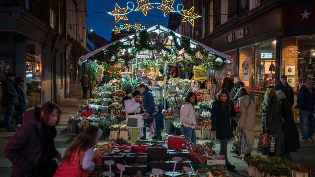 Stalls at York Christmas market at night, with star-shaped lights overhead and a flower seller tending to his busy stall 