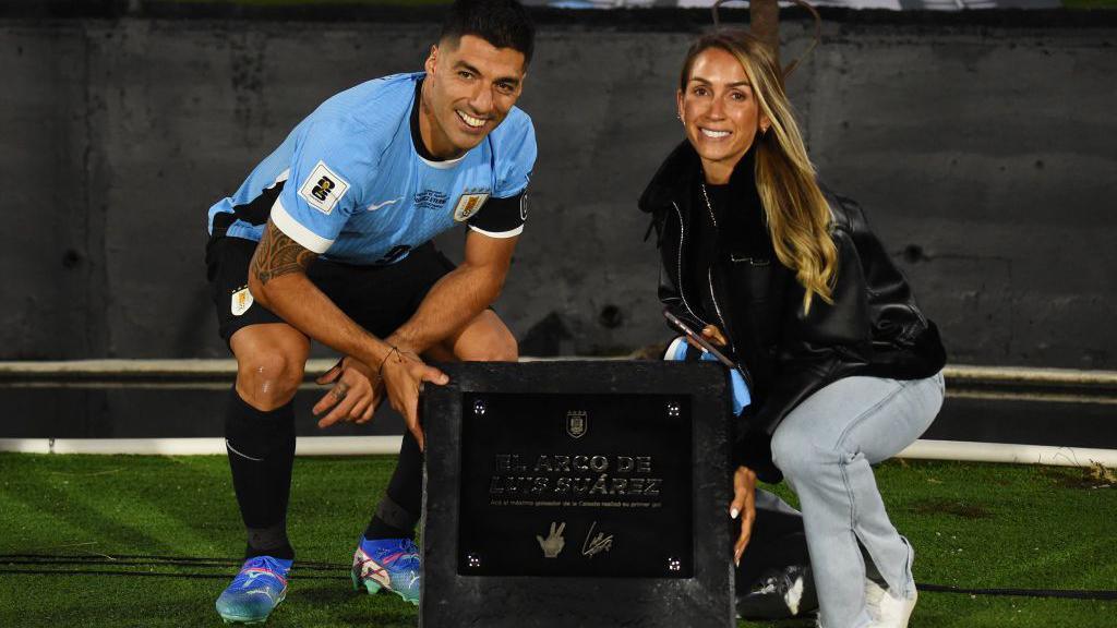 Luis Suarez and his wife posing with a plaque naming a goal net in his honour