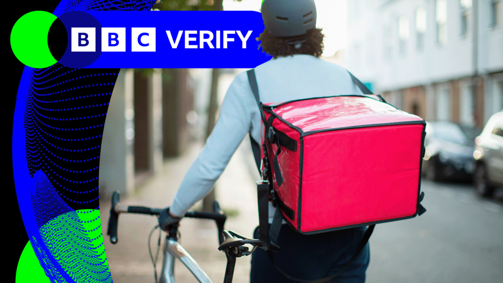 A food courier pushing a bike with a large red delivery box on his back