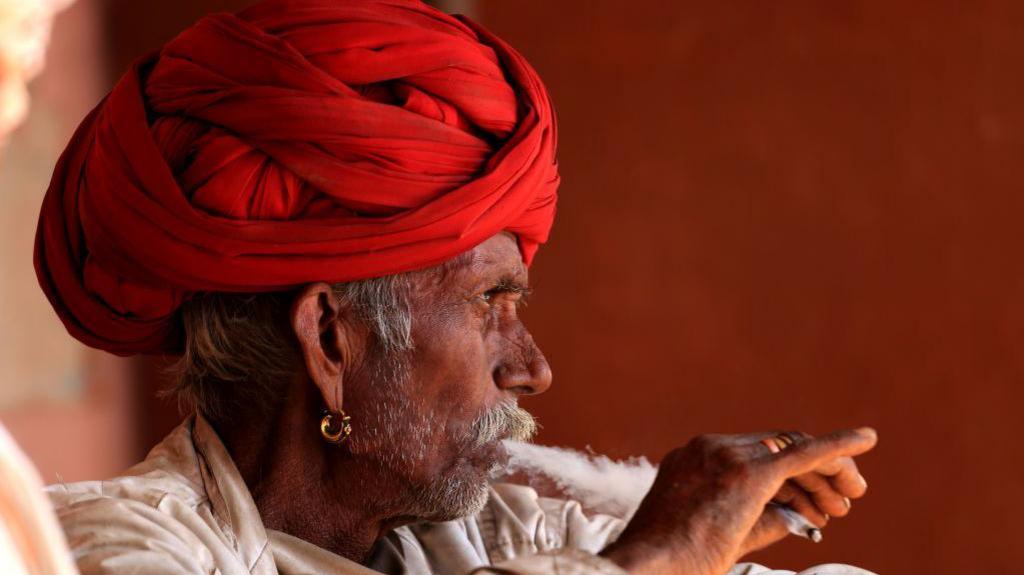 A man in a red turban smokes a cigarette