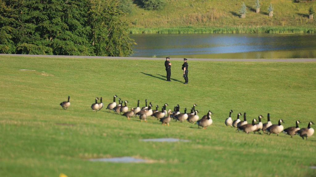 Swans in the foreground and two police officers next to one of Blenheim Palace's lakes