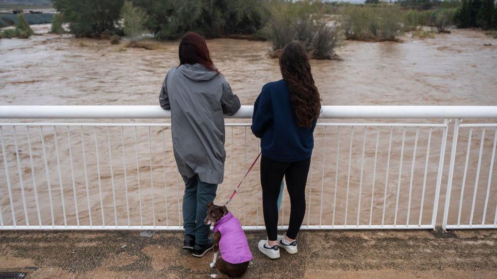 Two women and a dog look out over the flooded Magre River, in Valencia region - 30 October 2024