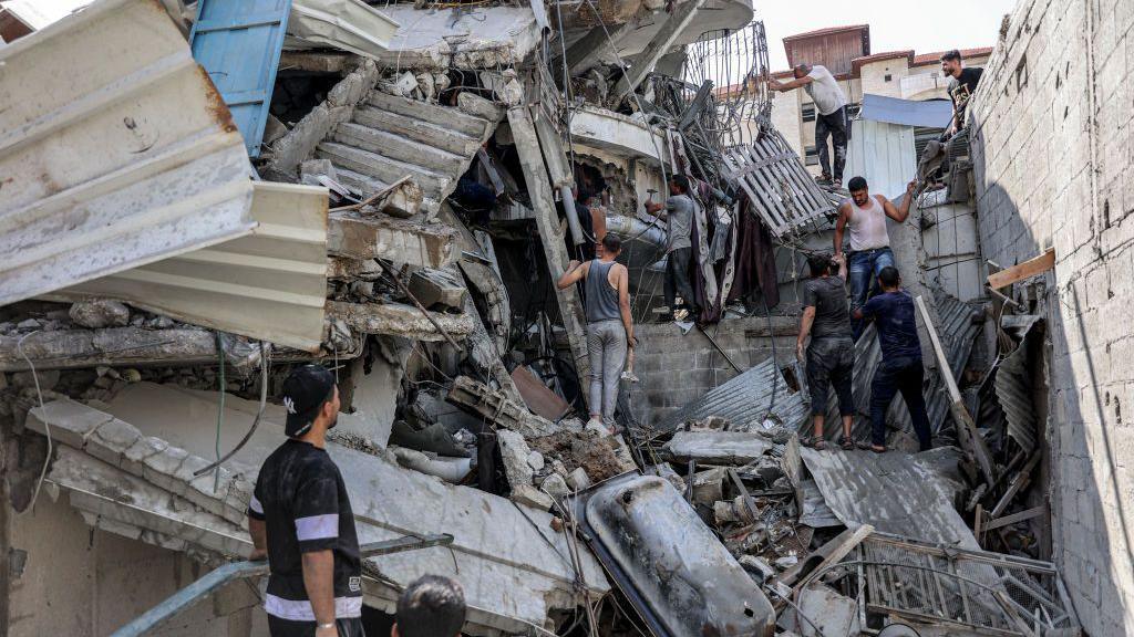 Palestinians attempt to rescue a man trapped underneath the remains of a building hit by Israeli bombardment, in the Saftawi district of Jabalia, in the northern Gaza Strip (15 October 2024)