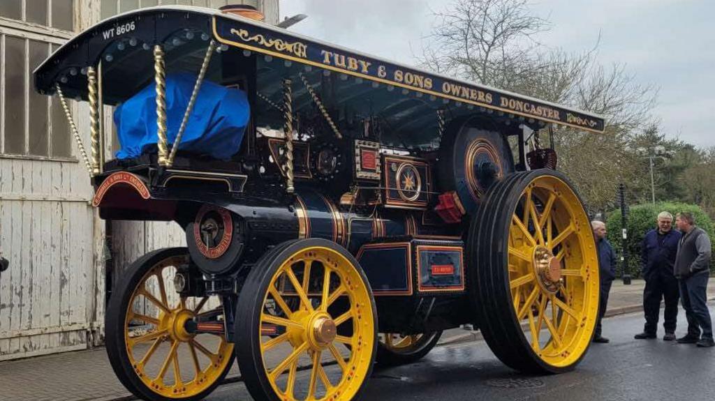 The Burrell showman's road locomotive is black with yellow wheels. It looks like a small steam train but has wheels and a canopy. 