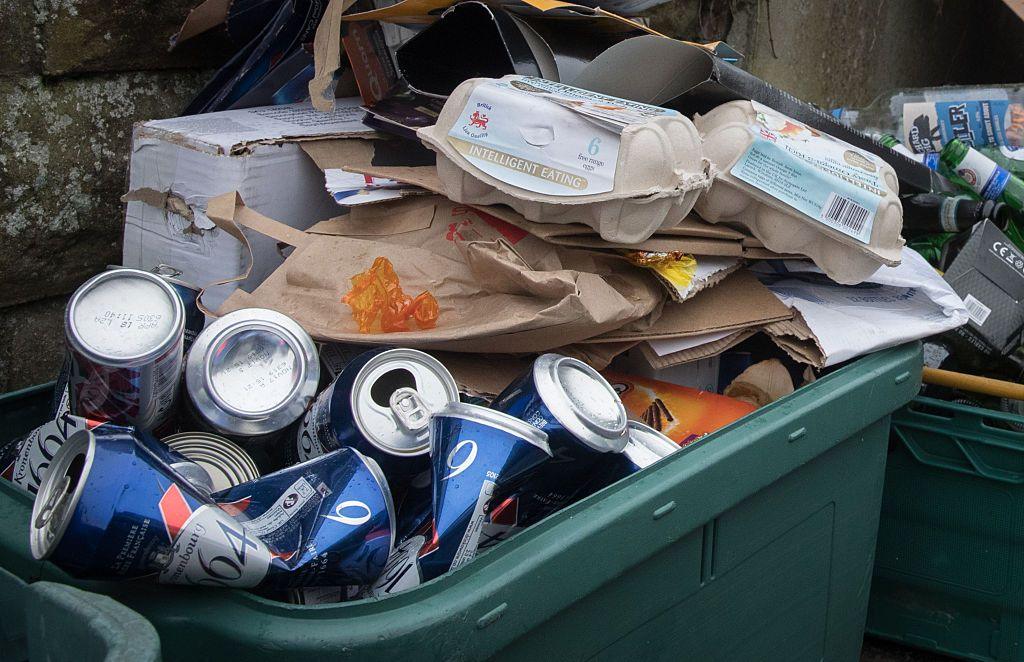 A full recycling bin with cans, cardboard and egg boxes.