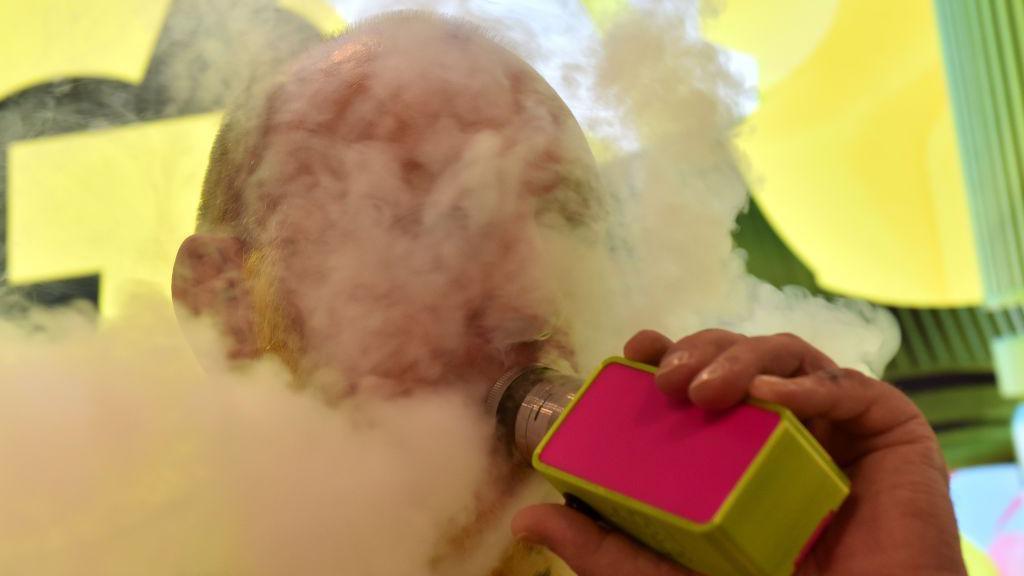A man is barely visible behind a massive plume of smoke from a plastic device he is smoking. 