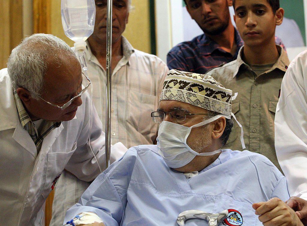 Megrahi speaks to a doctor at a hospital in Tripoli in September 2009. He is sitting on a wheelchair, wearing a medical gown and face mask.