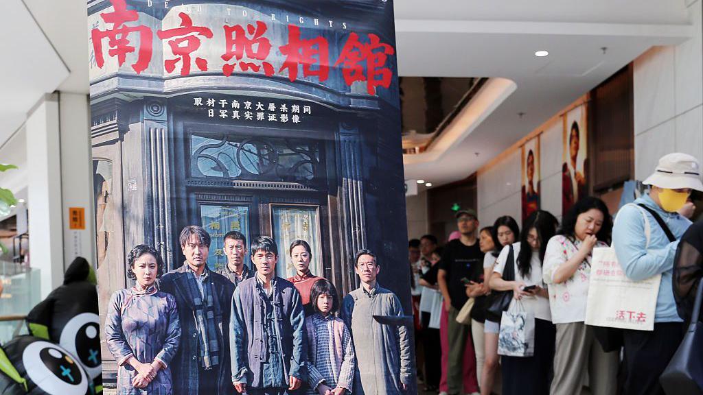 Movie fans queue by the promotional poster of the film "Dead To Rights" in the cinema