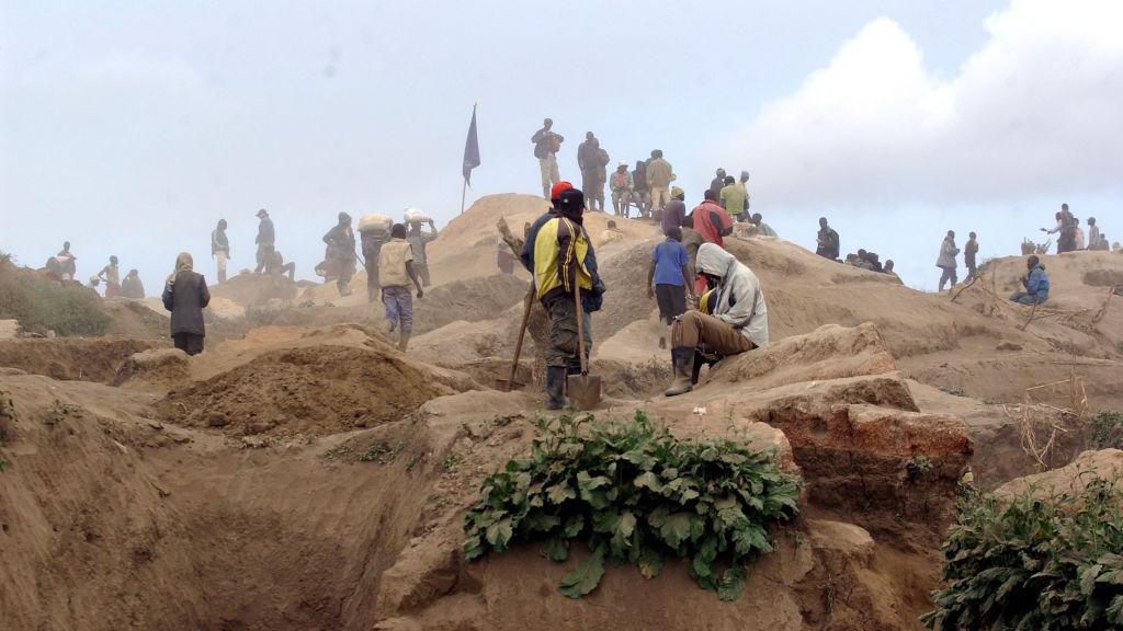 Dust swirls as miners sit atop a mining site shovels in hand.