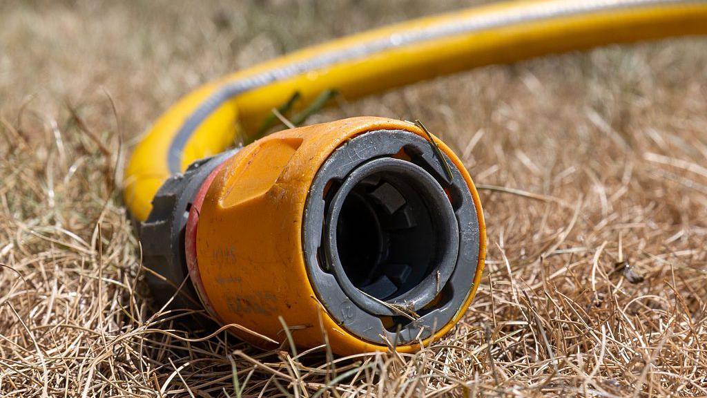 A hosepipe sits on brown dry grass