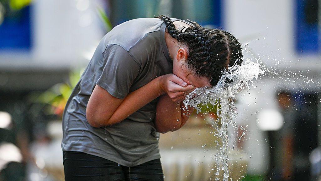 woman spashing water from a fountain on her face to cool down